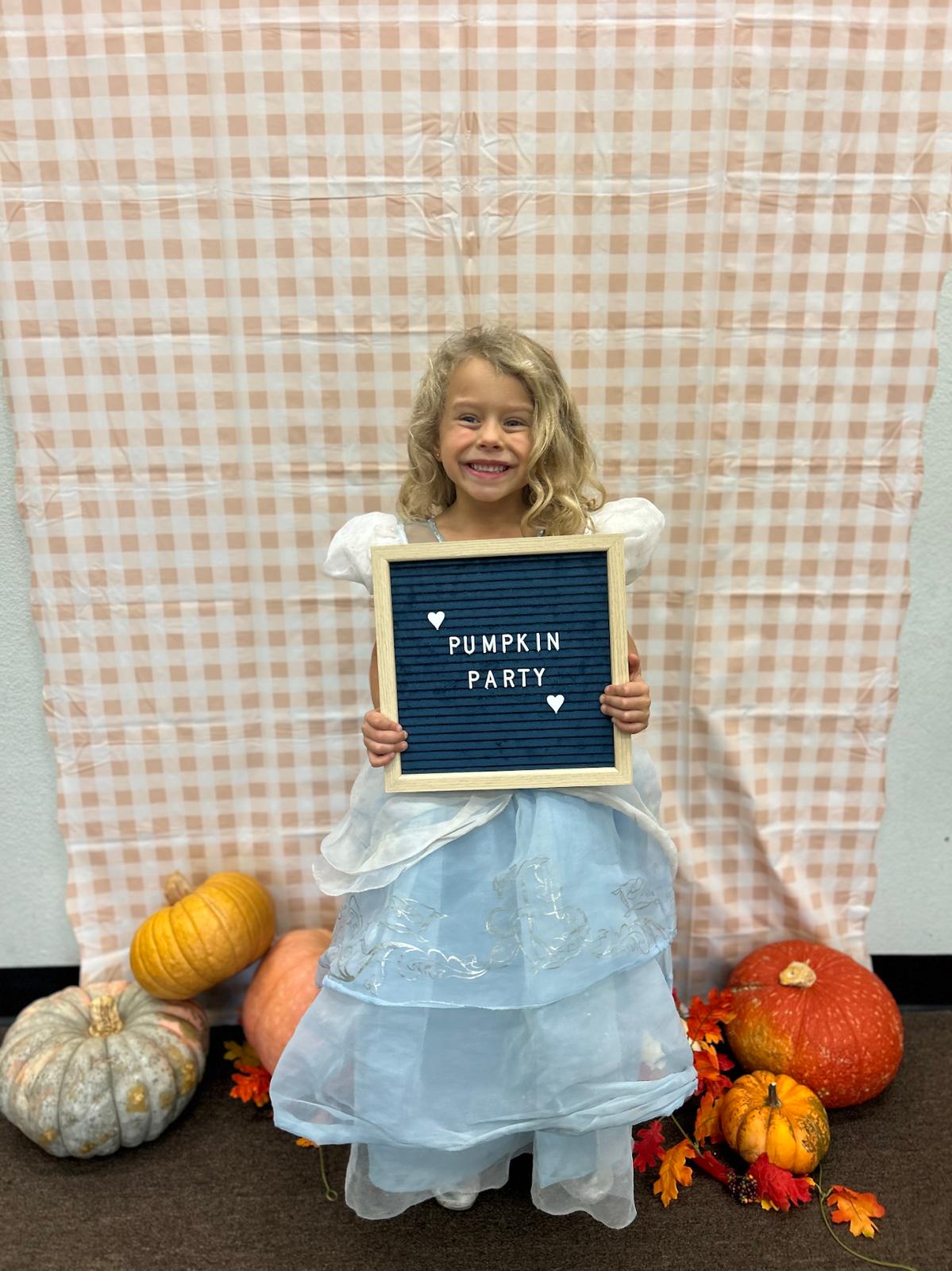 A dancer in a Cinderella costume holding up a Pumpkin Party sign, with pumpkins at her feet