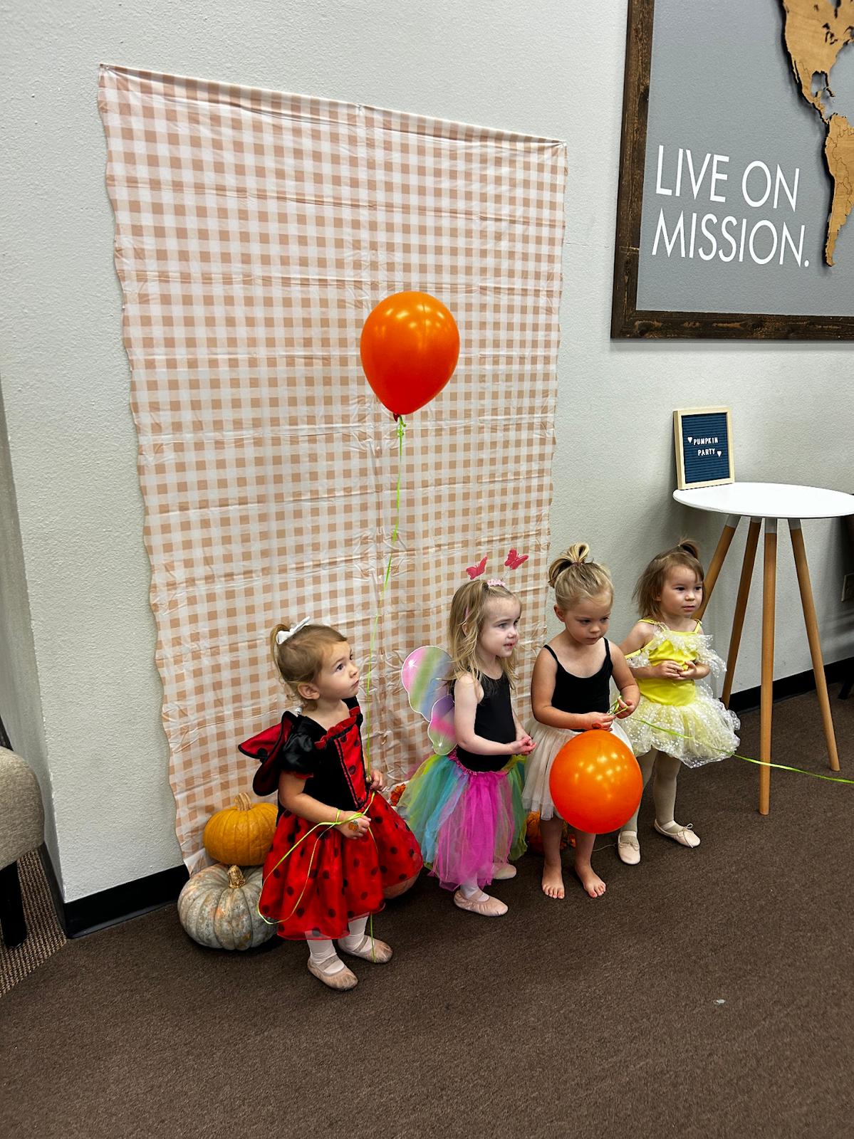 Three dancers in costume at the Pumpkin Party, with balloons and a pumpkin by the photo backdrop