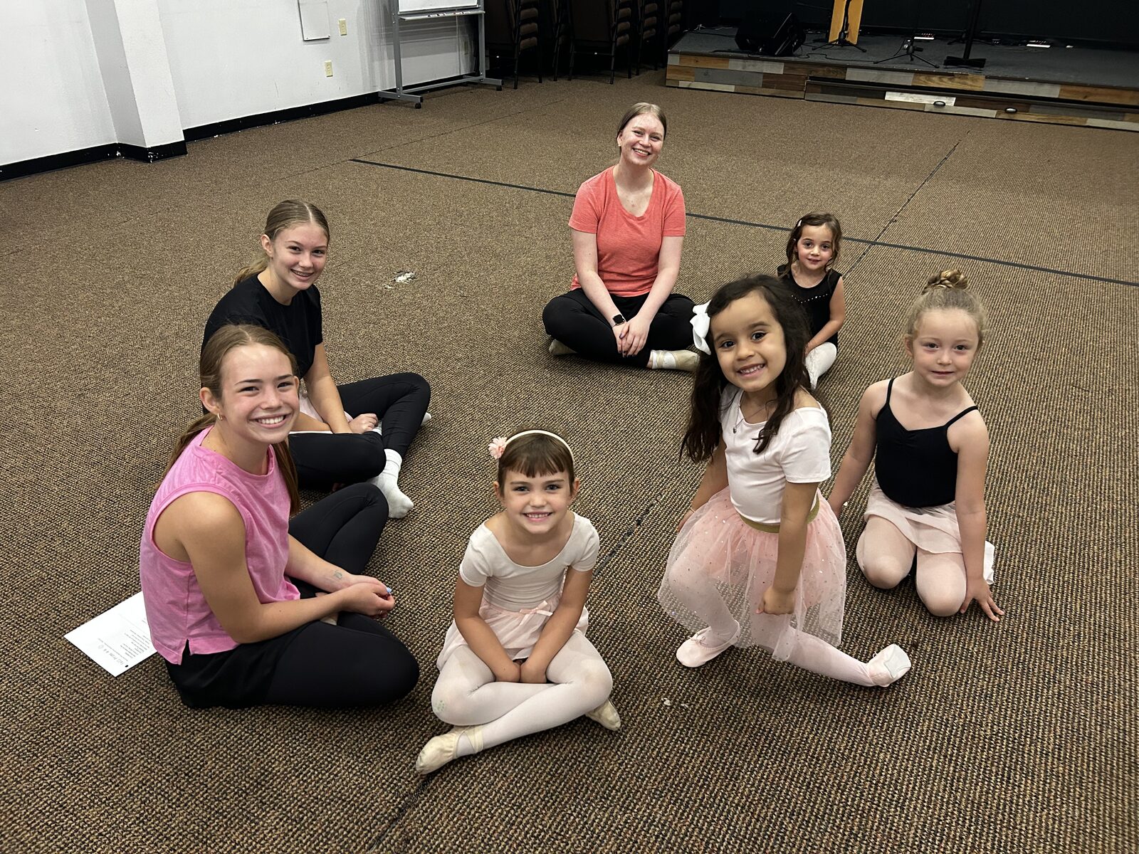 A class sitting on the Big Room floor with two teachers, ready to begin