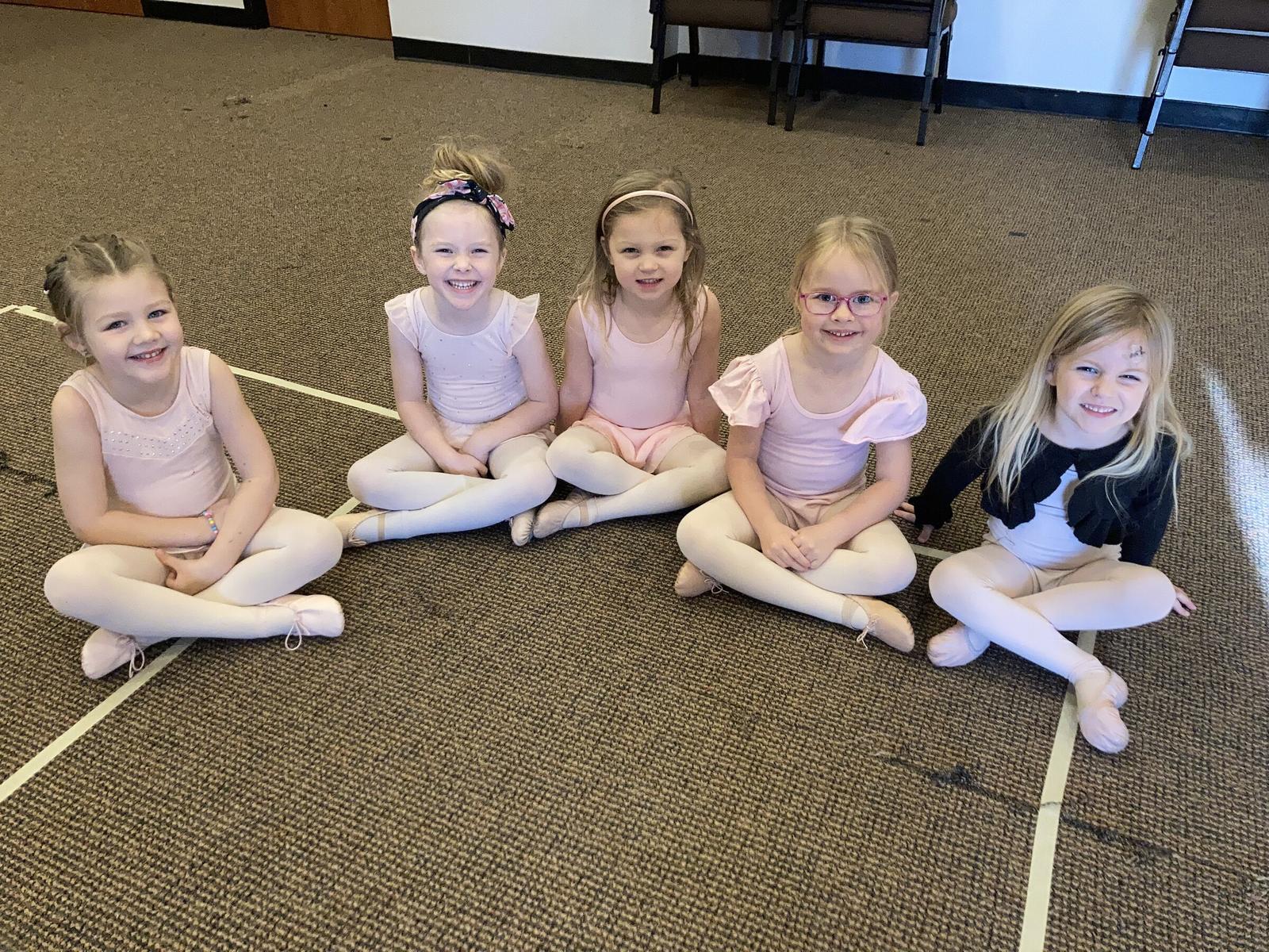 Five young dancers in pink leotards sitting cross-legged together on the Big Room floor